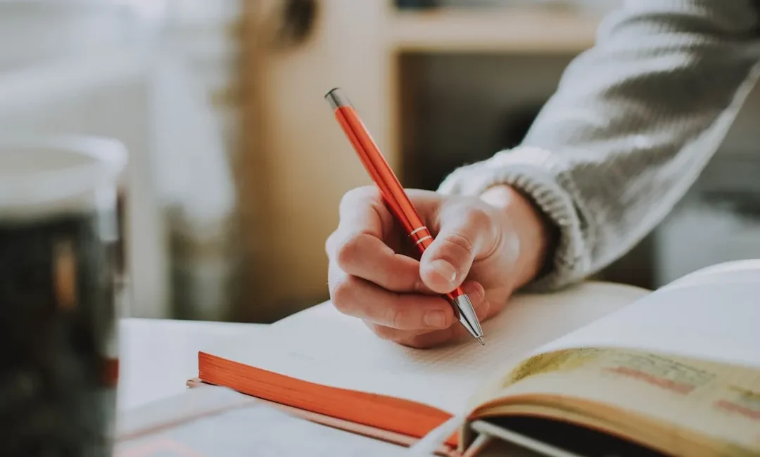 Hand schreibt mit Stift in ein Notizbuch – Schreiben vor dem Schlafen hilft beim Einschlafen
