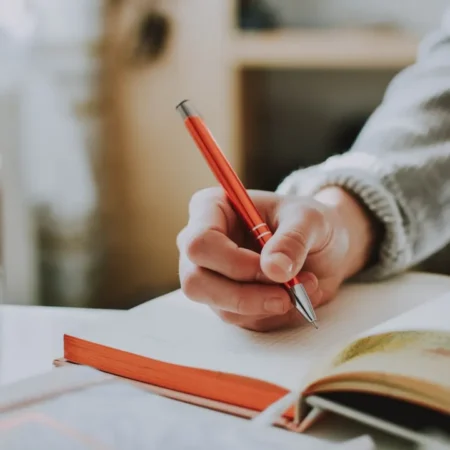 Hand schreibt mit Stift in ein Notizbuch – Schreiben vor dem Schlafen hilft beim Einschlafen