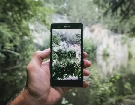 Person fotografiert einen See mit dem Smartphone – Apps für mehr Umweltschutz im Alltag